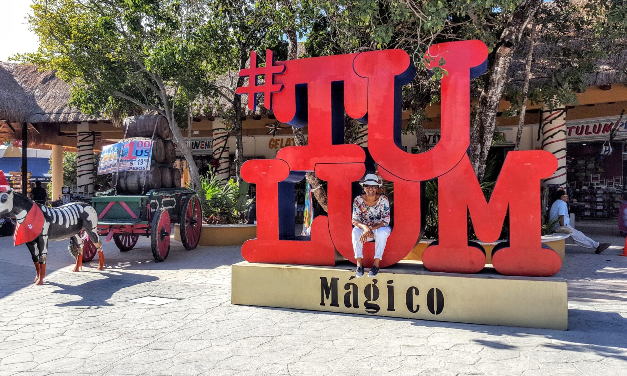 Woman in white pants sittign in front of Tulum sign in Mexico